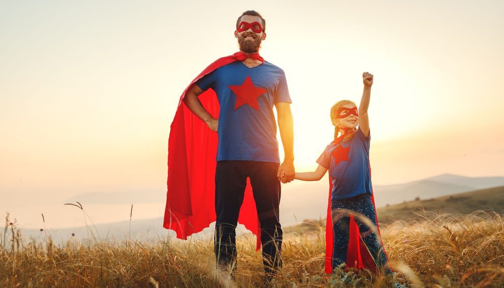 concept of father's day. dad and child daughter in hero superhero costume at sunset
